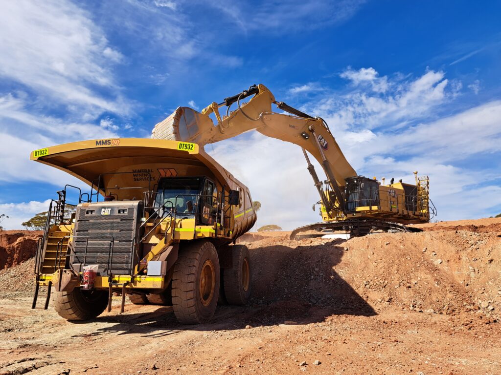MMS heavy‑mining equipment operating at a site in Western Australia with an articulated haul truck and excavator under clear sky.