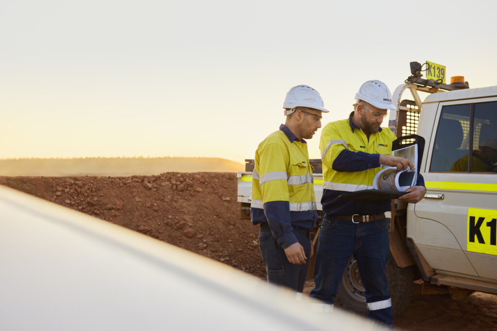 Mining supervisors from Mineral Mining Services review plans beside an MV on the job site at sunset in WA.